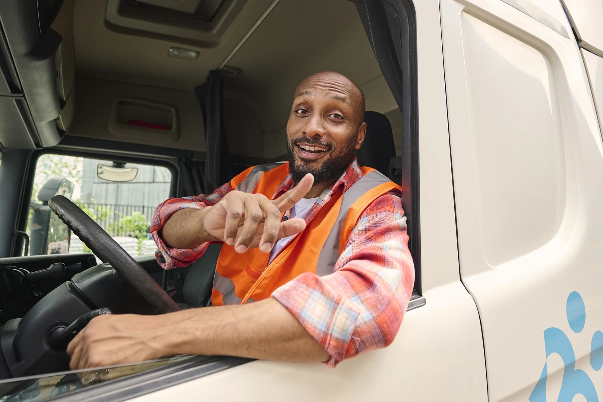 Kierowca ciężarówki w kamizelce odblaskowej uśmiecha się i wskazuje z kabiny — oferty pracy w transporcie z Accent